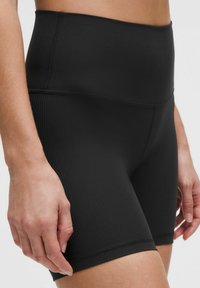 Pantalones cortos negros de cintura alta hechos de tela acanalada. Cintura elástica, forma ajustada y una textura suave con costuras cosidas.