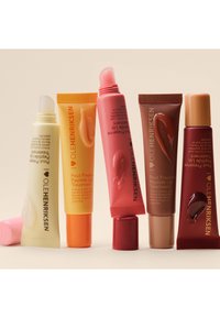 Cinque tubi di trattamento labbra in vari colori: giallo, arancione, rosa, rosso e marrone. Ognuno presenta un tappo a vite o a pressione con il nome del prodotto ben visibile.