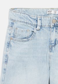 Jeans in denim azzurro chiaro con design a cinque tasche, chiusura con bottone metallico e tessitura slavata vicino alla vita e alle cuciture.