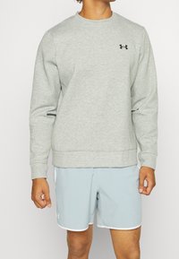 Light gray sweatshirt with long sleeves and a round neck, featuring a small black logo on the chest and side zip pockets.