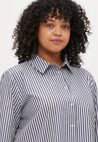 Striped button-up shirt in navy and white. Features a classic collar and a relaxed fit with a soft texture.