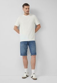 Witte T-shirt met korte mouwen gecombineerd met blauwe denim shorts. De outfit is compleet met witte sneakers en witte sokken. Eenvoudig design, geen patronen.
