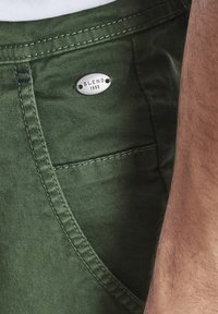 Şorturi din denim verzi, prezentând o buzunar pe partea dreaptă, cusături fine și un tab metalic cu inscripția "BLEND 1993" pe talie.