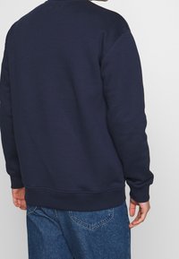 Sudadera azul marino con cuello redondo y puños acanalados, hecha de una mezcla de algodón, que presenta una textura suave y un diseño sencillo.