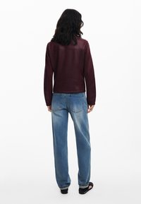 Burgundy leather jacket with a fitted design, smooth texture, and long sleeves, paired with loose blue jeans and black sandals.