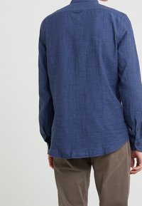 Koszula na guziki w ciemnym granacie, wykonana z teksturowanej tkaniny. Posiada długie rękawy, prosty dół oraz subtelny tylny karczek.