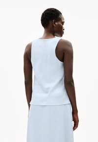 Light blue sleeveless top made of a smooth fabric, featuring a round neckline and a relaxed fit. Back has minimal detailing and no fastenings.