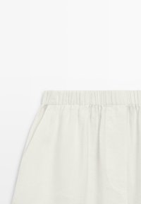 Weiße Hosen mit elastischem Bund und sichtbaren Seitentaschennähten vor einem schlichten weißen Hintergrund.