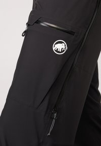 Schwarze Cargo-Hose aus leichtem Stoff, mit einer seitlichen Reißverschlusstasche, Zugband-Akzenten und einem weißen Logo eines Mammuts.