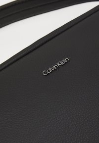 Black leather handbag with a structured design, featuring a textured surface and a silver Calvin Klein logo on the front.