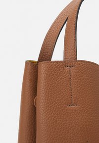 Hnědá kožená taška s texturovaným povrchem, dvěma pevnými uchy a viditelným švem. Nabízí živě žlutý interiér.