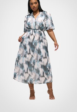 Vrouw draagt een midi-jurk met wolkenmotief in blauw, wit en grijs, met pofmouwen, knopen aan de voorkant en een gestrikte taille, gecombineerd met beige sandalen met bandjes.