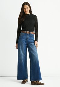Black knit long-sleeve top with textured pattern, high-waisted blue wide-leg jeans, brown belt, and snake-print flat shoes.