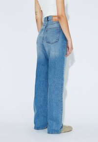 Light blue high-waisted jeans with a wide-leg fit, featuring back pockets and a brown label at the waistband. Textured denim material.