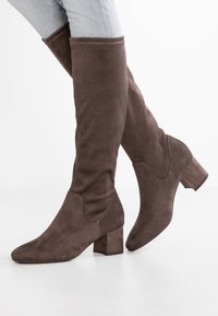 Botas altas de ante marrón hasta la rodilla con punta afilada y tacón cuadrado; presentan costuras decorativas a lo largo de la parte superior.