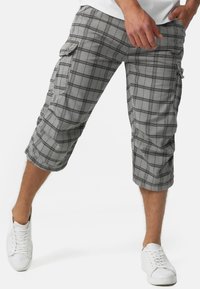 Grå rutede cargo-bukser med knælængde, der har lommer på siderne og et blødt, tekstureret stof, parret med hvide sneakers.