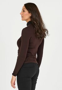 Camicia a maniche lunghe marrone con un design aderente e colletto nero testurizzato. Il tessuto è morbido, creando una silhouette e una struttura eleganti.
