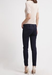 Sotilasnavy slim-fit -housut, jotka on valmistettu sileästä kankaasta, joissa on takataskut ja muotoillut saumat, yhdistettynä vaaleanbeigeen tiukasti istuvaan paitaan ja vaaleanbeigeihin korkokenkiin.