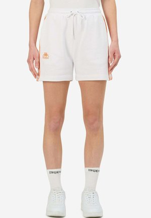 Shorts di cotone bianchi con strisce laterali arancioni e logo Kappa. Presentano una vita con cordino e un taglio rilassato. Indossati con scarpe da ginnastica bianche e calze.
