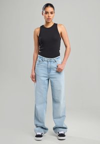 Black sleeveless top, light blue wide-leg jeans, and black sneakers. Smooth fabric, relaxed fit, visible stitching on jeans and contrasting accents.