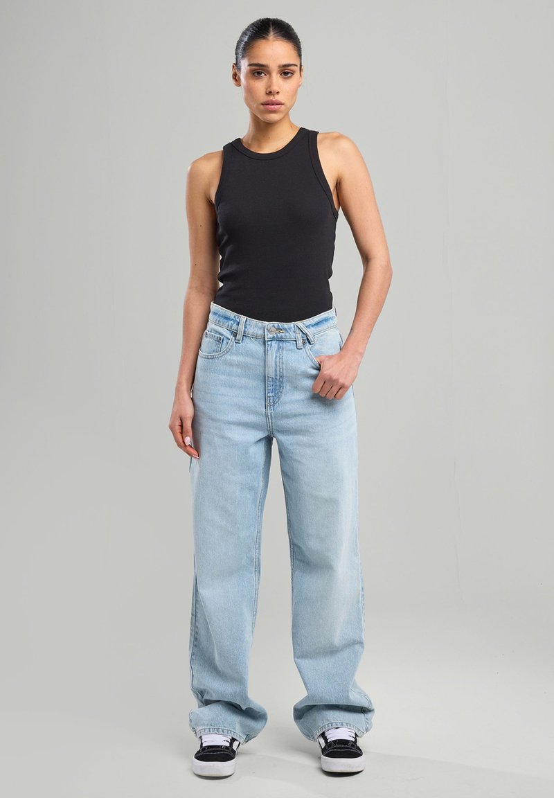 Black sleeveless top, light blue wide-leg jeans, and black sneakers. Smooth fabric, relaxed fit, visible stitching on jeans and contrasting accents.