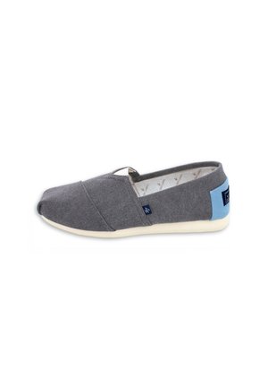 Zapato de lona gris tipo slip-on con parche azul claro en el talón y suela blanca, mostrado desde el lado derecho sobre un fondo blanco.