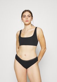 Black bralette with a square neckline and wide straps paired with matching black panties featuring a scalloped edge. Soft, stretchy fabric.
