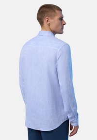 Camicia di lino azzurro chiaro con una vestibilità comoda, maniche lunghe, dettagli con bottoni sui polsini e una texture sottile. La vista posteriore mostra un orlo arrotondato.