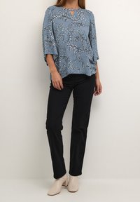 Blusa floreale blu con maniche a tre quarti e scollatura a chiave, abbinata a pantaloni neri e stivali con tacco a blocco beige chiaro.