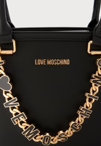 Schwarze Handtasche aus Leder mit einer goldenen Kettenriemen, verziert mit Buchstaben- und Herzakzenten. Das "LOVE MOSCHINO"-Logo in Gold ist über der Kette platziert.