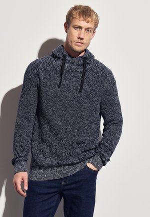 Donkerblauwe gebreide hoodie met een getextureerd patroon, kangoeroezak, trekkoord en geribbelde mouwen. Geloofd met een donkere jeans.