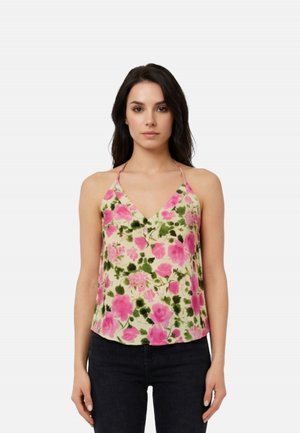 Donna che indossa una canotta senza maniche con scollo a V, decorata con fiori rosa e foglie verdi, abbinata a pantaloni neri, in piedi davanti a uno sfondo semplice.