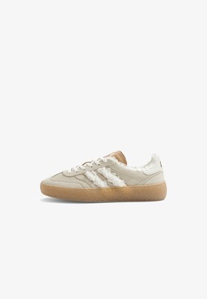 Baskets en daim beige avec des rayures blanches duveteuses et une doublure, des lacets blancs et une semelle en caoutchouc marron clair texturée.