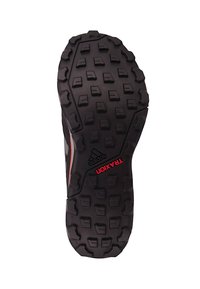 Black Adidas trail running shoe sole with aggressive treads for grip, featuring red "TRAXION" text and Adidas logo.