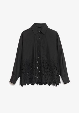 Svart skjorte med knapper som har en glatt overdel og en blondekant med blomstermerker. Kragen er strukturert, med perle-lignende knapper foran.