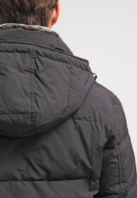 Czarna ocieplana kurtka z kapturem, pikowanym wzorem i miękką podszewką z polaru wzdłuż kołnierza. Wyraźne przeszycia jako akcent.