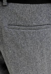 Grå ullbukser med én baklomme, glatt tekstur og skreddersydd passform. Stoffet virker varmt og lett teksturert.