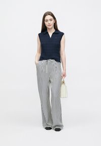 Mornarsko plava majica bez rukava s teksturiranim uzorkom i ovratnikom, uparena s crno-bijelim širokim hlačama na pruge. Bijela torbica.