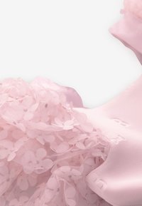 Vaaleanpunaisen mekon yksityiskohta, jossa on kerroksittain läpikuultavaa kangasta, jossa on kukkakirjailuja ja kimaltavia koristeita. Yläosassa sileää satiinikangasta.