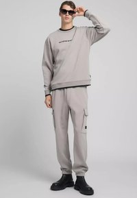 Felpa grigio chiaro e pantaloni cargo abbinati, entrambi in tessuto morbido. La felpa presenta un logo nero; i pantaloni hanno tasche laterali e polsini a costine.