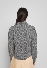 Floral print blouse with a black background, featuring small multicolored flowers, a collar, and puffed sleeves. Hemline is slightly curved.