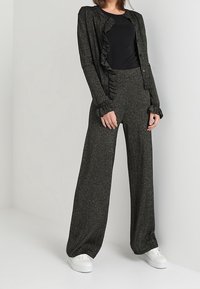 Zwart-zilverachtige getextureerde outfit met een cardigan met ruches en wijde broeken, gecombineerd met witte sneakers.