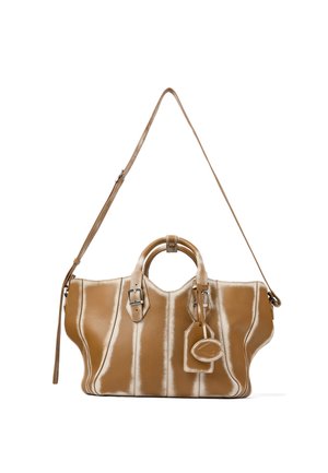 Handtas van lichtbruin leer met bovenhandvatten, verstelbare schouderriem, riemen met gespen en een aangehecht bagagelabel tegen een witte achtergrond.