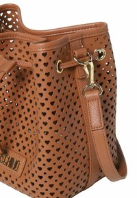 Bruine leren handtas met hartvormige uitsparingen, gouden hardware accenten en een verstelbare schouderriem. Met een gestructureerde en zachte afwerking.