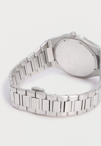 Ασημένιο μεταλλικό ρολόι χειρός με συνδεδεμένο μπρασελέ, που δείχνει το πίσω μέρος της θήκης και το κούμπωμα σε λευκό φόντο.