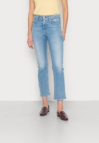Jeans en denim bleu avec une coupe droite, taille mi-haute et ourlet brut, associés à des chaussures à enfiler bordeaux. Lavage clair avec un léger délavage.