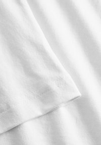 White cotton fabric with a smooth texture, displaying a folded edge and stitching detail along the hem. No patterns or accents present.