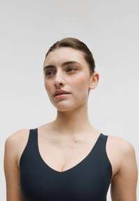 Bañador negro con un diseño de escote en V profundo, tirantes delgados y textura suave. La tela parece elástica y se ajusta al cuerpo.