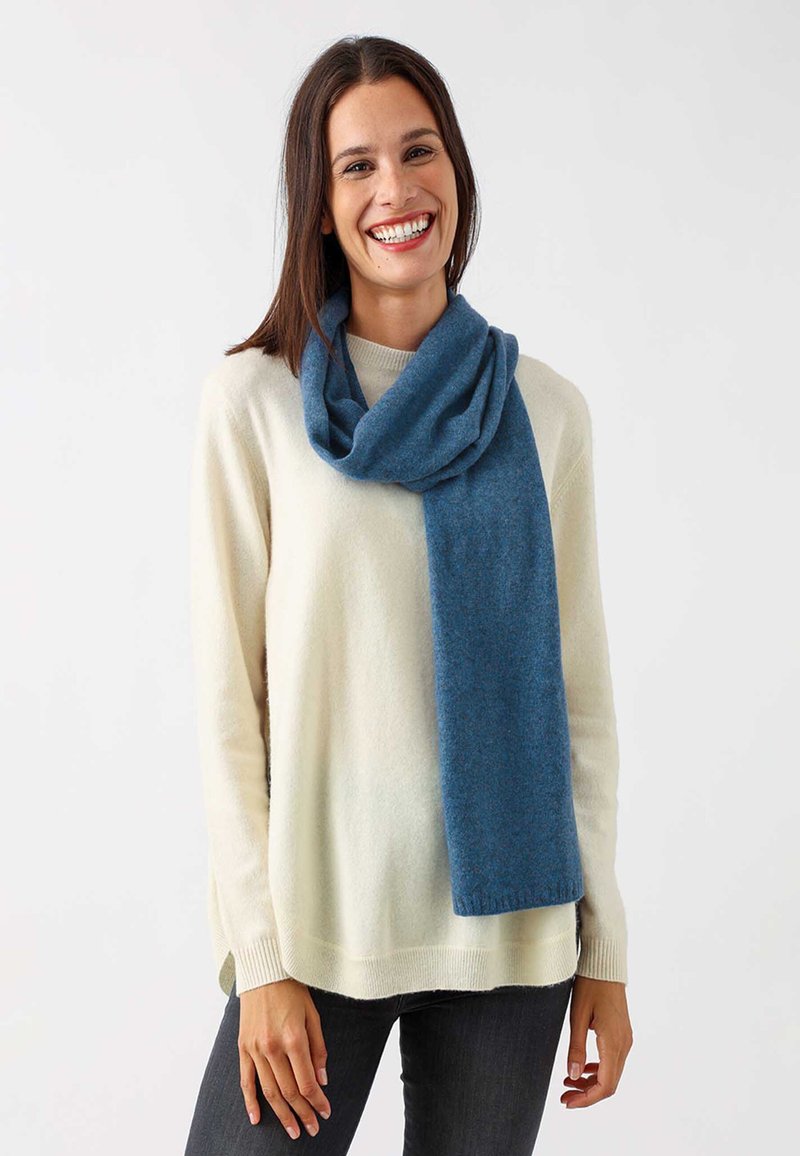 Blauer Schal aus weichem, strukturiertem Stoff, locker um den Hals drapiert, kombiniert mit einem hellen cremefarbenen Pullover und dunklen Jeans.