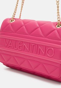 Quiltad rosa handväska med det präglade "Valentino"-logotyp, kedjesträng i guldton och trekantig mönsterdetaljering.